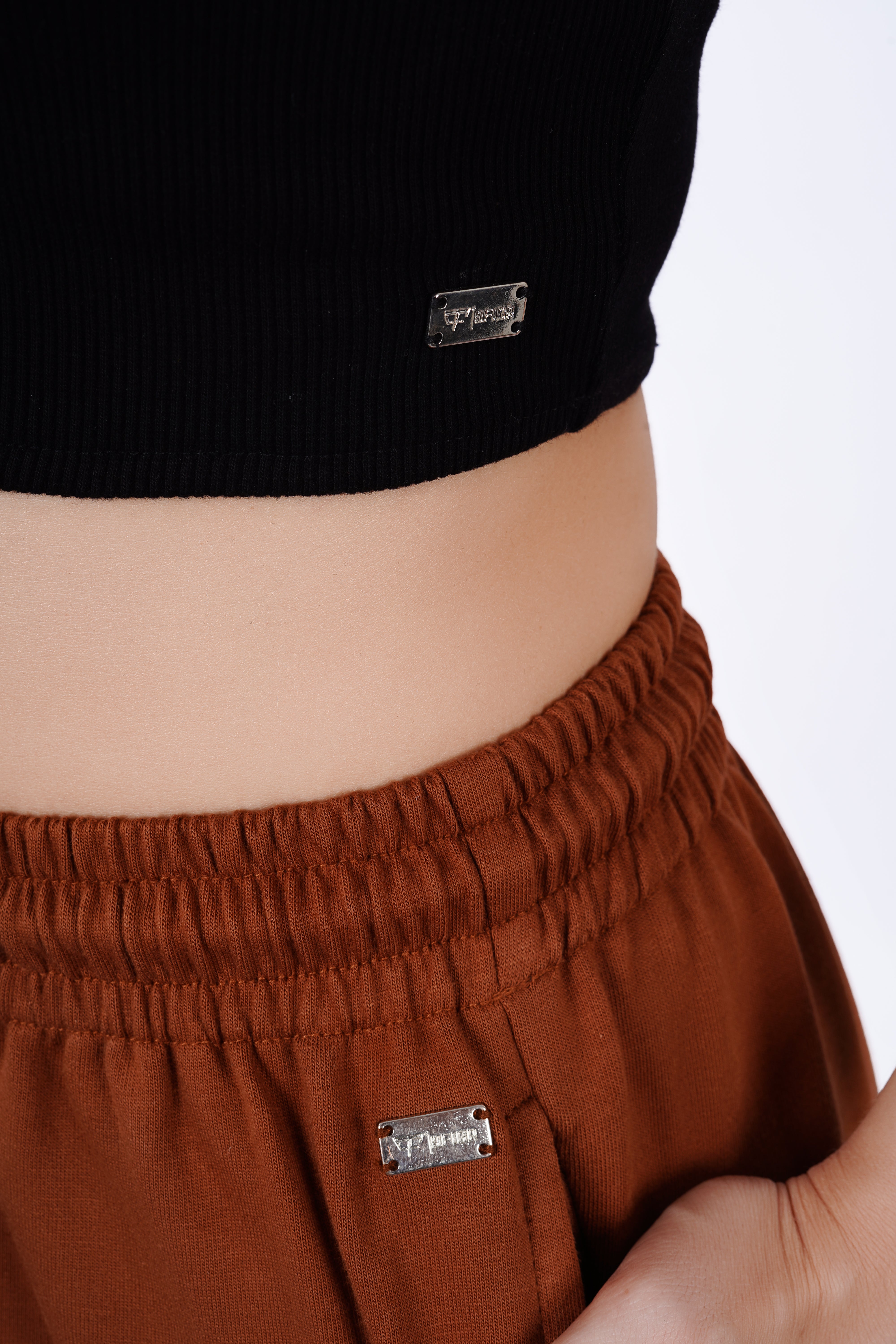 Person wearing brown pants and a black top with visible brand labels.
