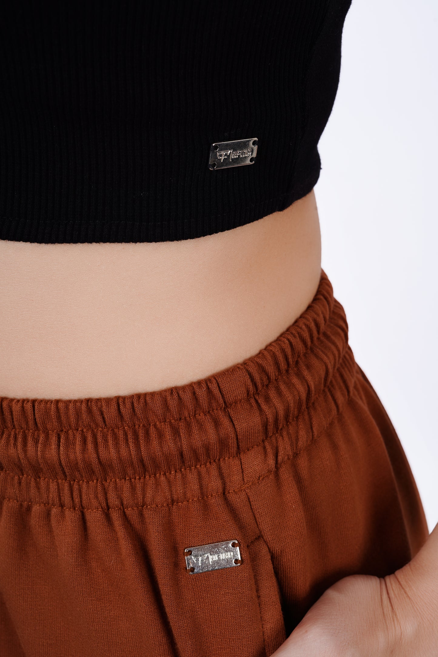 Person wearing brown pants and a black top with visible brand labels.
